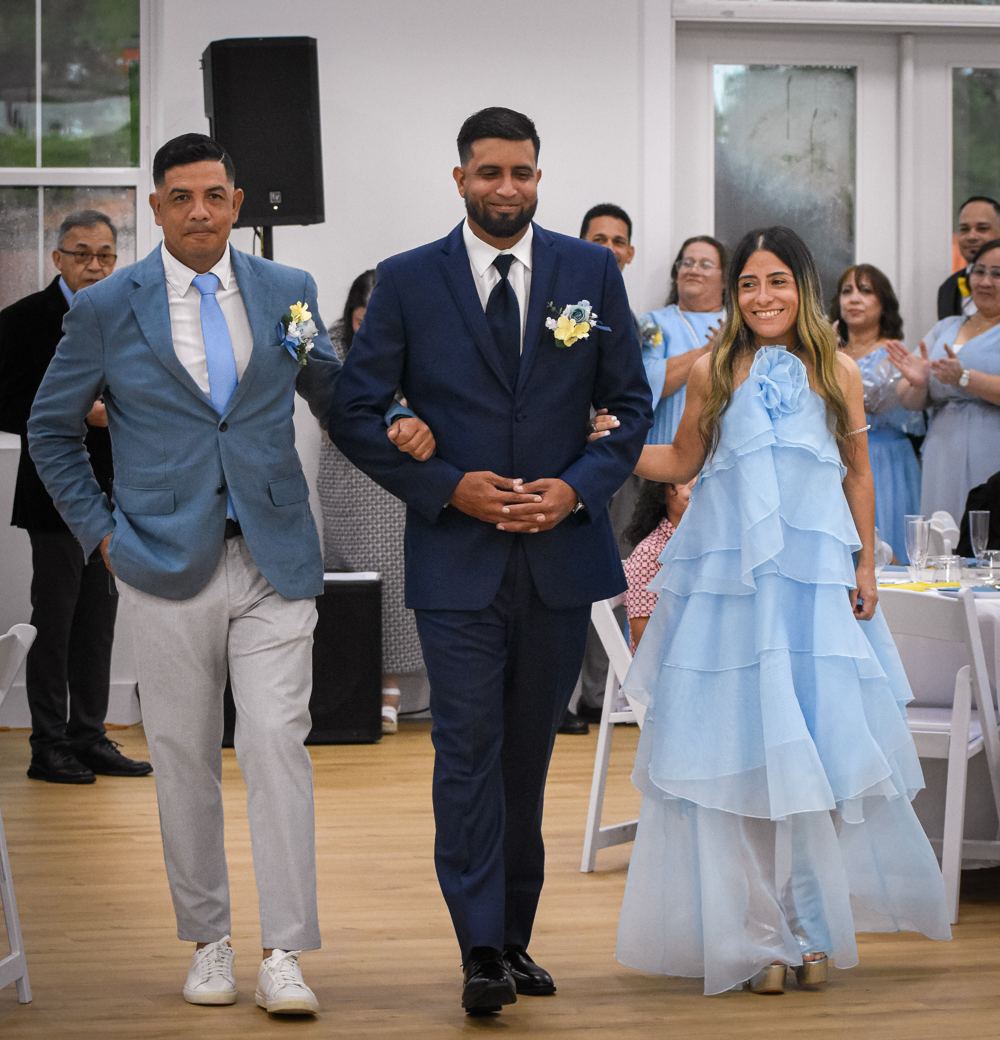 Novio entrando a la recepción del brazo de sus acompañantes mientras los invitados aplauden