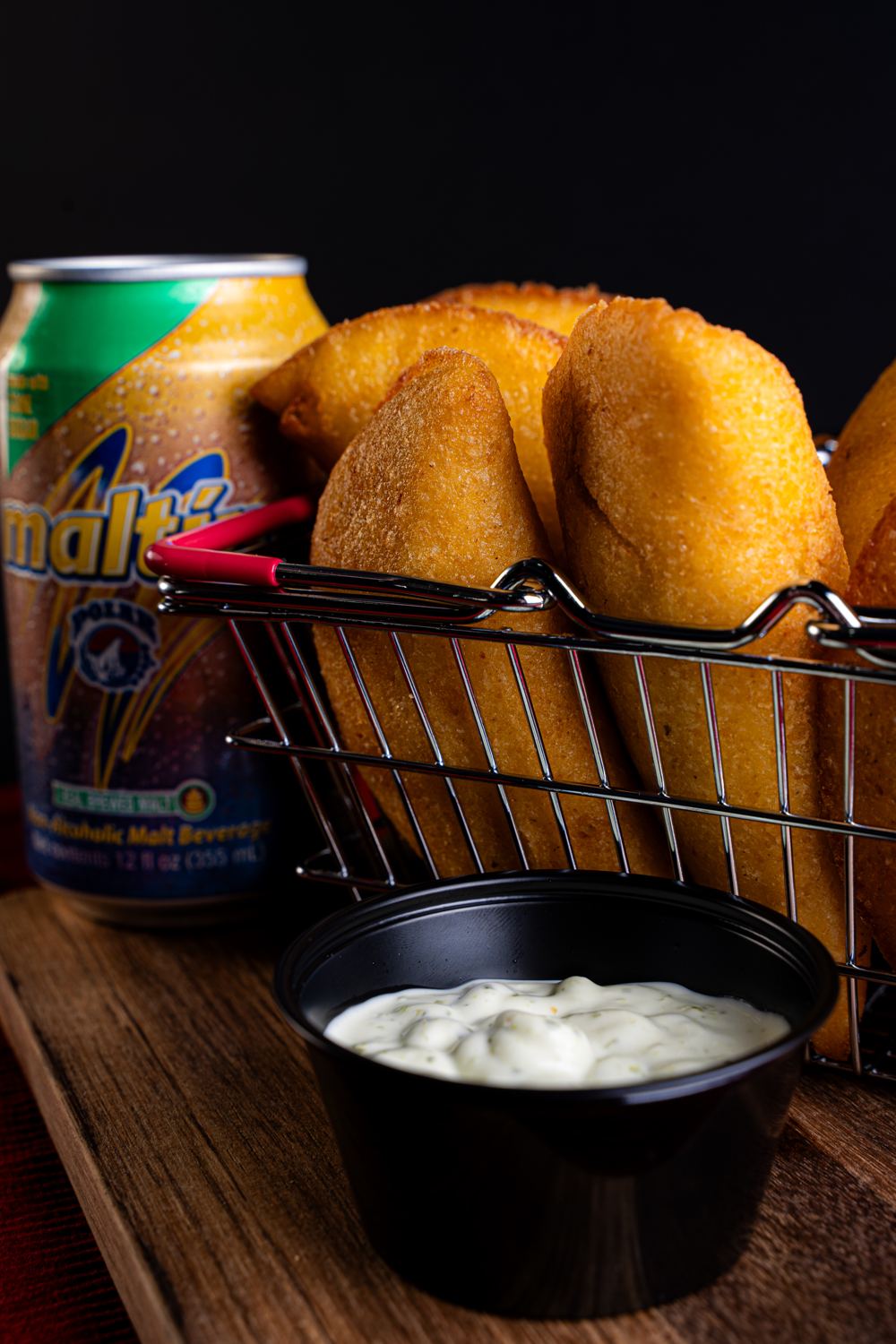 Empanadas en una canasta metálica con salsa y una malta