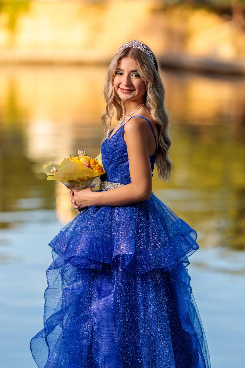 Quinceañera con vestido azul de tul junto al agua al atardecer